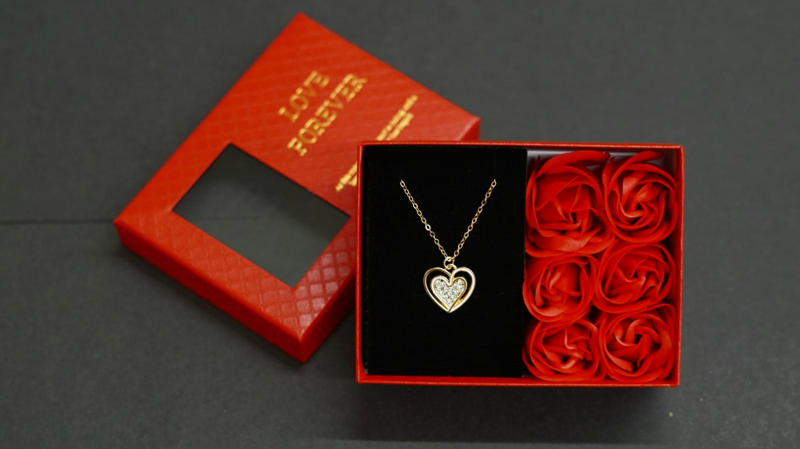 Love Forever heart pendant necklace set in a red gift box with decorative artificial flowers.
